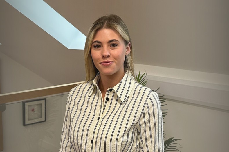 Portrait of a young woman with blonde hair in a striped button-down shirt, in a modern office.